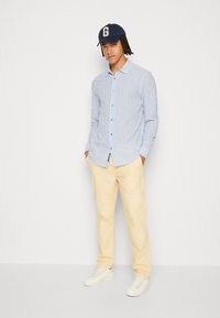 Camisa de cuadro azul claro y blanca, combinada con pantalones color crema y zapatillas blancas. El modelo lleva una gorra azul marino.