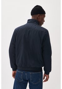 Tamsiai mėlynas bombonešis su aukštu apykakle, elastingomis rankovėmis ir juosmeniu. Lygus, tekstūruotas audinys, laisva forma. Derinamas su džinsais.