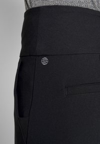 Černé kalhoty se hladkým povrchem, s malým bílým logem globusu na zadní straně a jedním detailem kapsy.