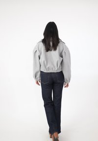 Grå, tekstureret pullover med puffede ærmer, kombineret med mørke denimjeans. Har en kortere kant og figursyet talje.