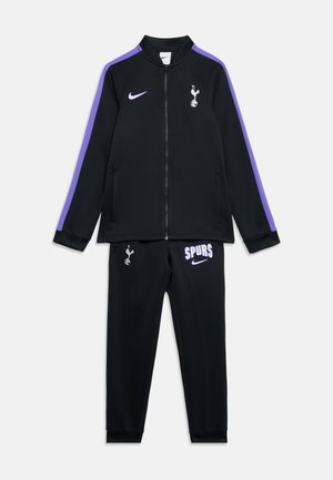Schwarzer Tottenham Hotspur Trainingsanzug mit violetten Streifen an den Ärmeln und Hosen, Jacke mit Reißverschluss, Nike- und Spurs-Logos auf Brust und Oberschenkel.