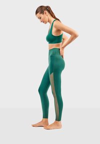 Groene sportbeha en high-waisted legging met meshpanelen. Getailleerd ontwerp, gladde textuur en naadloze constructie.