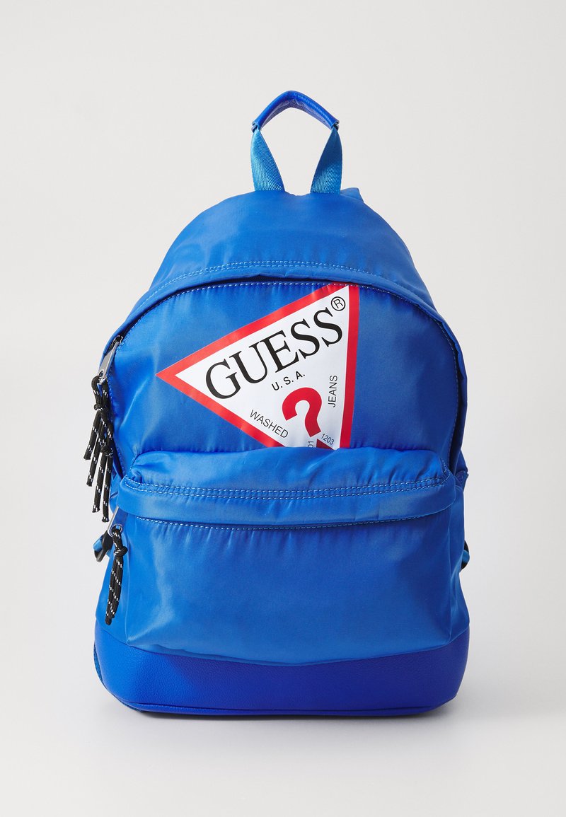 Sac à dos en nylon bleu avec un logo rouge triangulaire, des tirettes de fermeture éclair noires et une poignée sur le dessus. Dispose de bretelles rembourrées et d'une poche avant.