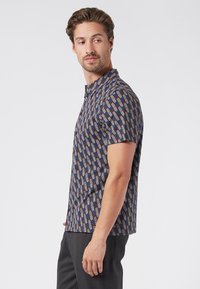 Polo de manga corta con un patrón geométrico en tonos azul, rojo y beige. Hecho de material transpirable con cuello abotonado.