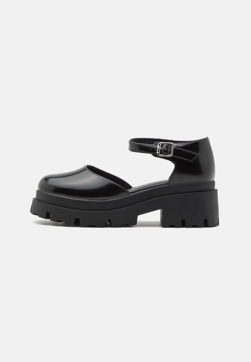 Chaussure Mary Jane à plateforme noire avec semelle épaisse à crampons et boucle de bride autour de la cheville, finition lisse, vue de profil sur fond uni.