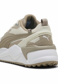 Μπεζ και λευκό αθλητικό παπούτσι Puma με υφασμάτινο άνω μέρος με υφή, παχύ μαξιλαρωμένο πέλμα, λουρί στο πίσω μέρος και λογότυπο Puma στο πλάι και στη φτέρνα.