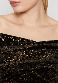 Tessuto di velluto nero con motivi a stelle dorate; texture liscia con un design drappeggiato e scollatura a spalle scoperte.