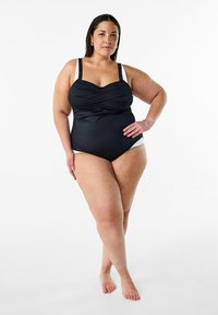 Costume intero nero con arricciature sul corpetto, spalline regolabili e dettagli bianchi sui fianchi. Tessuto liscio e elastico.