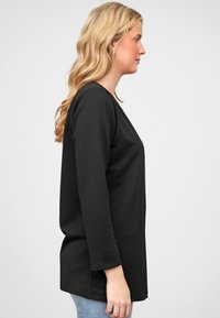 Zwart langemouwen top met een gestructureerd, geribbeld ontwerp. Rechte snit, ronde halslijn en zijsplitten, gecombineerd met lichtblauwe jeans.