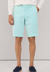 Pantalones cortos de color azul claro hechos de algodón, con un frente plano, bolsillos laterales y dobladillos enrollados, combinados con zapatos oscuros de tela sin cordones.