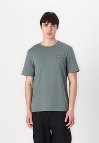 Camiseta verde de manga corta hecha de algodón suave, con un escote redondo y un pequeño logo amarillo bordado en el lado izquierdo del pecho.