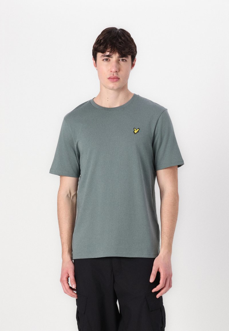 Camiseta verde de manga corta hecha de algodón suave, con un escote redondo y un pequeño logo amarillo bordado en el lado izquierdo del pecho.