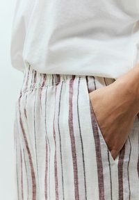 Páskové lněné kalhoty s uvolněným střihem, s vertikálními pruhy v červené, černé a bílé barvě. Elastický pas a boční kapsa jsou viditelné.