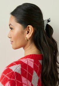 Röd och rosa mönstrad tröja med en diamantdesign, prydd med ett svart och vitt leopardmönstrat hårsnodd och guldiga hoops.