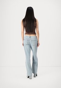 Brun rynket croptopp, lyseblå vide denimjeans, teksturert stoff, enkelt design, vist bakfra med langt svart hår.
