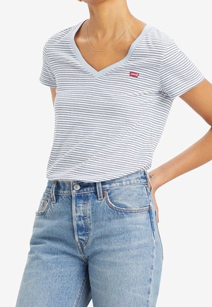 Osoba nosząca biało-granatowy pasiasty T-shirt Levi’s z dekoltem w serek, włożony w jasnoniebieskie dżinsy z wysokim stanem, z srebrnym naszyjnikiem.