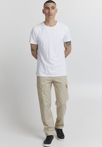 T-shirt en coton blanc associé à un pantalon cargo beige avec des poches latérales, et des baskets noires avec des semelles blanches. Design simple et décontracté.