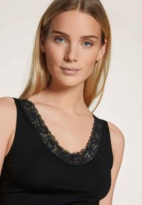 Zwarte tanktop met een V-hals afgewerkt met kant. De stof lijkt glad en heeft een aansluitende pasvorm, waardoor de kantdetails langs de halslijn worden benadrukt.
