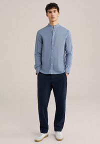 Svetlo modra srajca z dolgimi rokavi, s pokončnim ovratnikom, z gumbi spredaj, v kombinaciji z mornarsko modrimi hlačami ter belimi supergami. Gladek material in sproščen kroj.