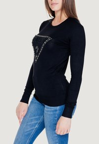 Maglione nero a maniche lunghe con un design a logo triangolare arricchito di strass sul davanti. Polsini e orlo a coste. Texture liscia.