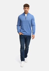 Lyseblå striktrøje med høj krave og kvart-zip, pyntet med mørke jeans og hvide sneakers. Glat tekstur og tætsiddende design.