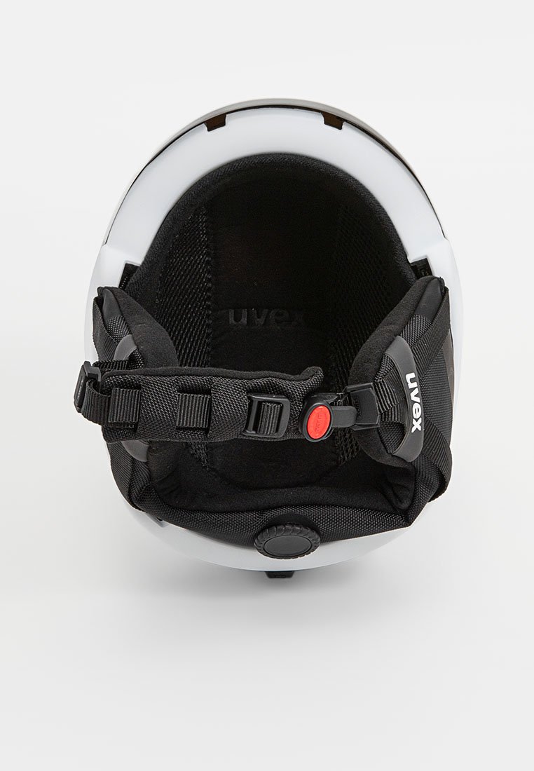 Schwarz-weißer Helm mit gepolstertem Innenleben, verstellbaren Riemen und einem roten Knopf zur Größenanpassung. Materialien bestehen aus Kunststoff und Stoff.