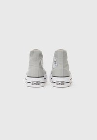 Gray canvas high-top sneakers with white rubber soles, black stripes, and a circular logo patch on the outer side.