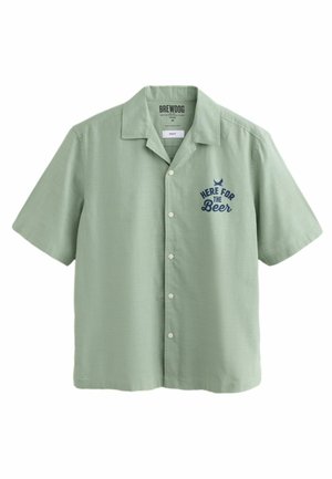 Camisa de botones de manga corta verde claro con cuello y texto en azul marino "Aquí por la Cerveza" en el lado izquierdo del pecho.