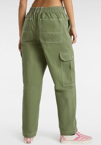 Grüne Cargo-Hosen mit elastischem Bund, Front- und Gesäßtaschen sowie kontrastierendem weißen Nähten, kombiniert mit rosa karierten Sneakers.