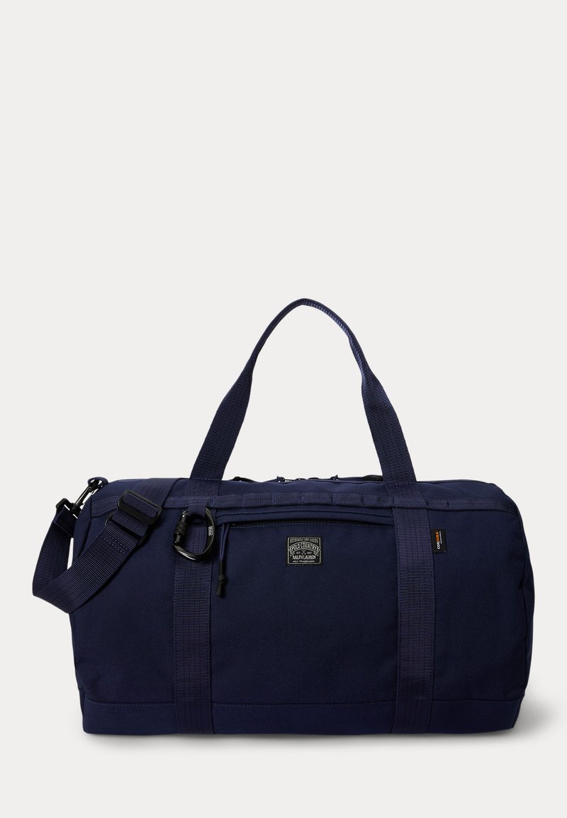 Sac polochon bleu marine avec double poignée, bandoulière ajustable, poche avant zippée et petit écusson logo au centre.