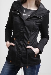Czarna lekka kurtka z kapturem, zapinana na zamek z przodu, ze ściągaczem w talii i dwoma przednimi kieszeniami. Posiada drewniane troczki i teksturowaną tkaninę.