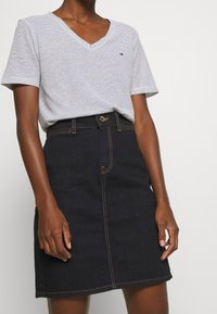 T-shirt a V con righe grigie e bianche abbinato a una gonna a matita in denim scuro. La gonna presenta cuciture in vista e una chiusura con bottone.