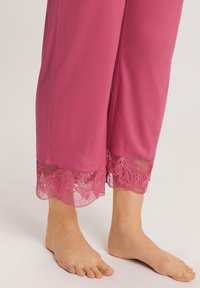 Rosa loungebyxor med en smidig textur, prydda med spetsdetaljer i fållarna, som visar blommönster och genomskinliga inslag.