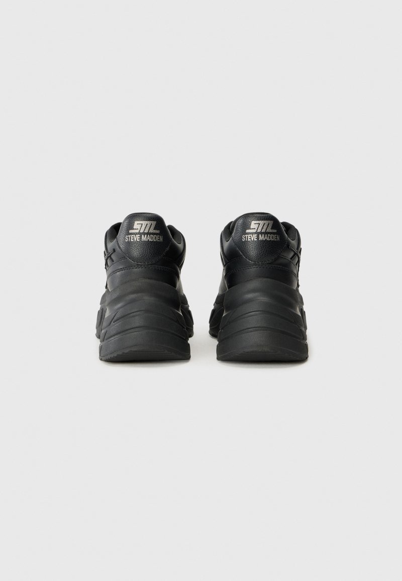 Des chaussures de sport noires avec une tige synthétique texturée, un bout arrondi et une semelle en caoutchouc épaisse et ondulée. Présente le logo argenté au niveau du talon.