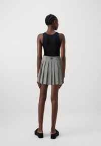 Top fitted nero abbinato a una mini gonna a pieghe a scacchi bianco e nero. Le scarpe sono sandali neri con zeppa. Design semplice, texture liscia.