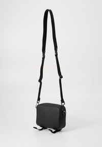 Black synthetic crossbody bag with a rectangular shape, zipper closure, adjustable strap, and minimalistic design. Features two bottom straps.