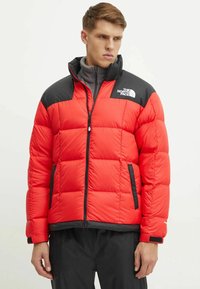 Giacca puffer rossa con accenti neri sulle spalle, zip frontale e tasche laterali. Presenta un design a trapunta e il logo The North Face sul petto.
