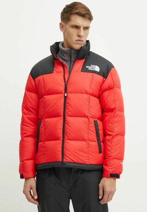 Chaqueta acolchada roja con acentos negros en los hombros, cremallera frontal y bolsillos laterales. Presenta un diseño acolchado y el logo de The North Face en el pecho.