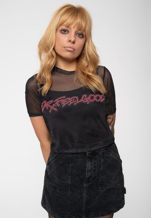 Black cropped top with short sheer sleeves and red "DR. FEELGOOD" text, paired with a high-waisted black denim skirt featuring front pockets.