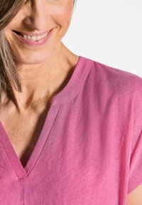 Leichtes pinkes V-Ausschnitt-Oberteil mit kurzen Ärmeln, das einen entspannten Schnitt und eine subtile Textur aufweist. Eine Naht entlang des Ausschnitts fügt Details hinzu.