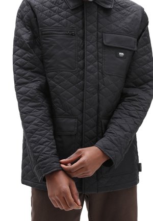 Veste matelassée noire avec plusieurs poches avant, dont une poche zippée et un patch logo Vans sur la poche poitrine, portée par une personne.