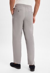 Graue Hose mit glatter Textur, elastischem Bund und zwei Gesäßtaschen, im gerade geschnittenen Stil. Schwarze Schuhe runden das Outfit ab.