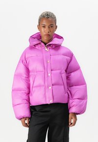 En lys rosa puffjakke med en boksform, gullfargede detaljer og hette. Den har store quiltede seksjoner og frontlommer.