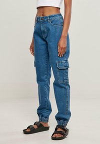 Pantalones cargo de mezclilla azul con puños elásticos y múltiples bolsillos laterales. Presenta una cintura con cierre de botón y detalles de costura clásica.