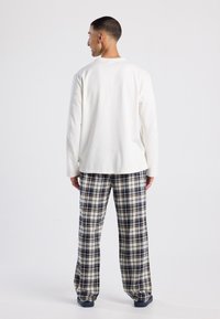 Wit katoenen overhemd met lange mouwen, gecombineerd met geblokte loungebroeken in marineblauw, crème en beige. Losse pasvorm, rechte snit, zachte textuur.