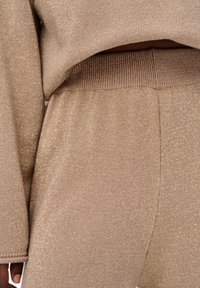 Beige gebreide outfit met een subtiele glans. Voorzien van een geribde tailleband en manchetten, met een zachte textuur en een aansluitend ontwerp.