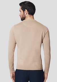 Beżowy sweter z długim rękawem, z ribbowanymi mankietami i dołem. Gładka struktura z okrągłym dekoltem, prezentowany z tyłu.