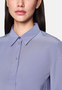 Light purple shirt with a collar, featuring a button-down front and smooth, textured fabric. Includes a discreet button closure at the collar.