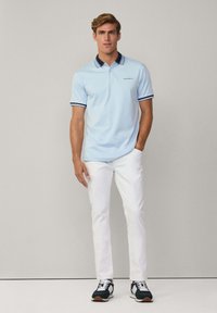 Světle modrá polo košile s námořnickými detaily a logem, spárovaná s bílými kalhotami a tmavými teniskami. Hladká textura a klasický střih.