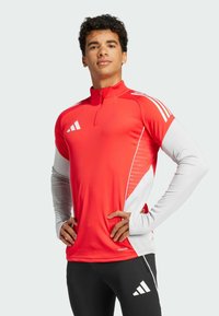 Rød atletisk langærmet top med kvart lynlås, hvide ærmer og sidelæns paneler med et subtilt gradientmønster. Tre-stribe logo på skuldren.